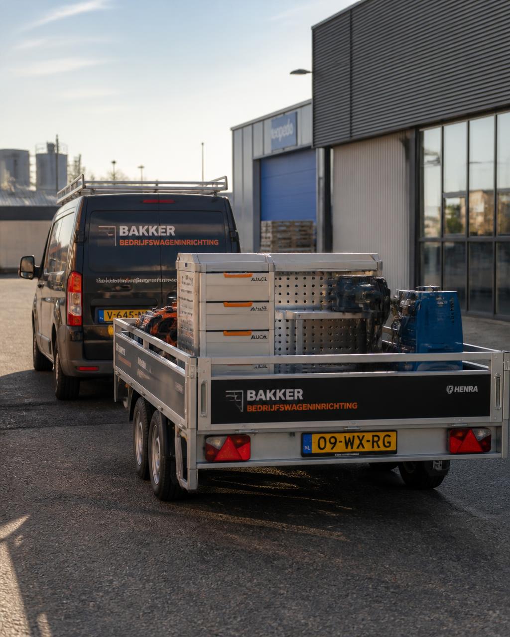 Bedrijfsaanhangwagen met materiaal achter een bestelbus op een bedrijventerrein
