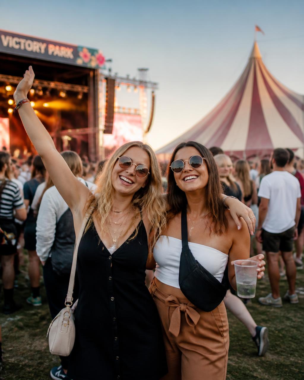 Bezoekers op een openluchtevenement met podium en feesttent in de avondzon